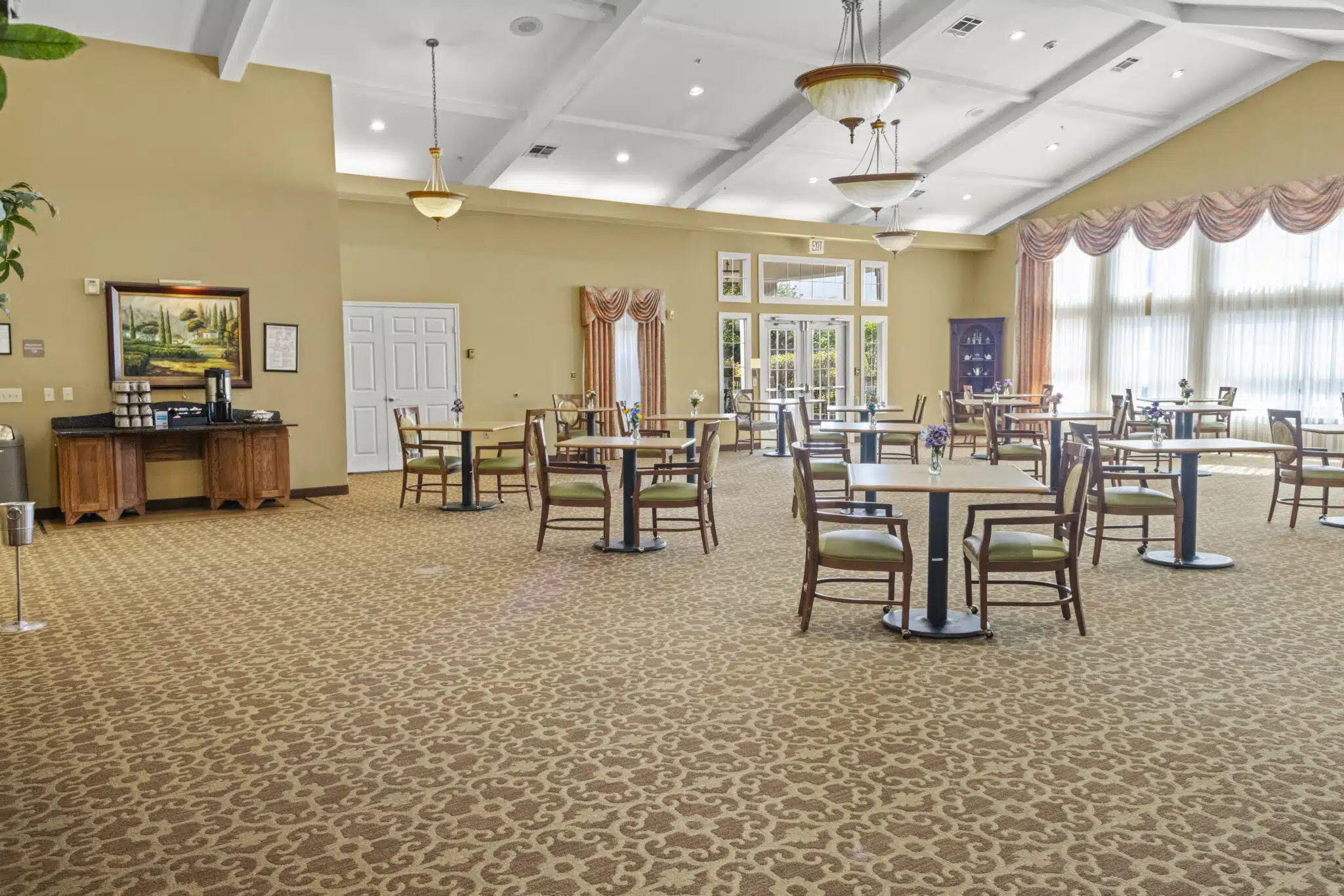 A second photo of the dining hall taken from a separate corner of the room. It includes views of the tables, chairs, exit, bank of windows. Included in this pic is a coffee bar station.