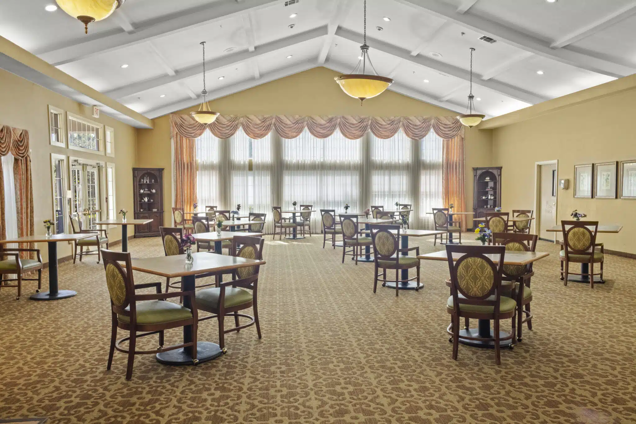 Large, spacious dining hall with 16 2-person tables. There is a set of French doors for exiting. The room has a bank of windows on the far side and room is decorated with built-in hutches.