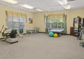 Spacious rehabilitation Gym, with a few exercise machines, various weights, massage table, and mirror.