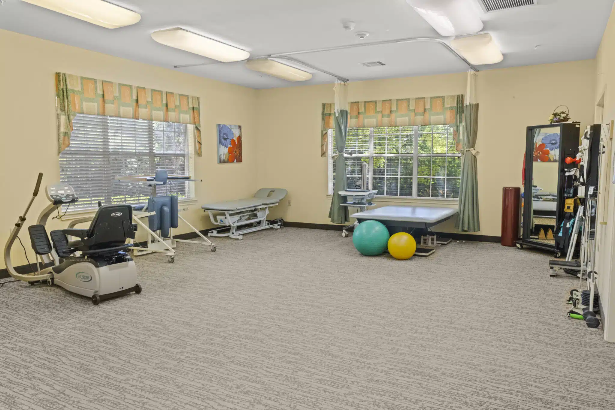 Spacious rehabilitation Gym, with a few exercise machines, various weights, massage table, and mirror.