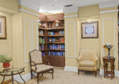 Facility library/study with two floor-to-ceiling bookshelves and two chairs with decorative end tables.