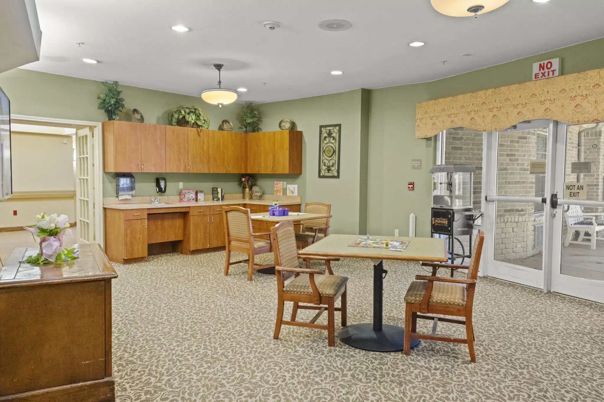 Photo of another lounge area located near an exit. In the room are two sets of tables with chairs, upper and lower cabinets located near an L-shaped hutch.
